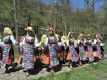 a long chain of Bulgarian girls "Lazarki" with geometric aprons, yellow scarves and flowers on their heads.