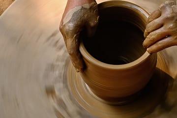 dark hands turning a clay pot on a wheel