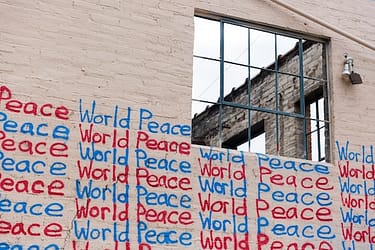 The skeleton of a brick building painted white, with many lines of words written on it "world peace world peace"